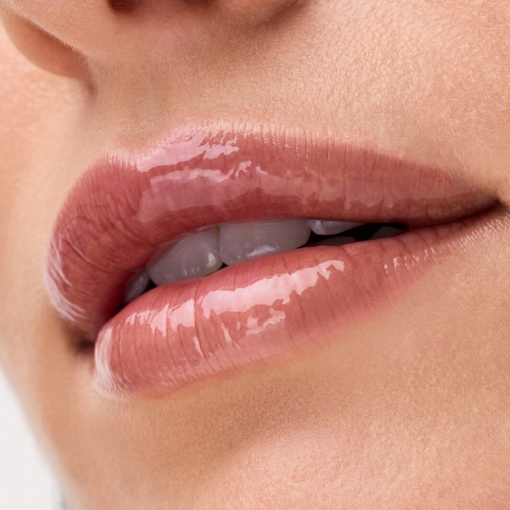 Gros plan sur des lèvres avec un baume à lèvres brillant. Peau claire, teinte rosée.