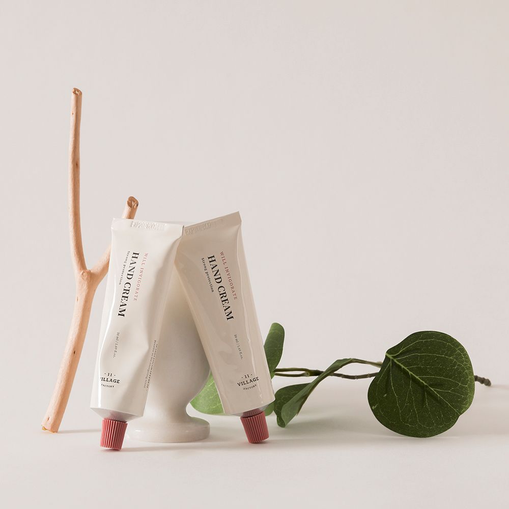 Deux tubes de crème. Texte: HAND CREAM, WILL INVIGORATE, .11 VILLAGE FACTORY. Bouchons roses. Branche, feuille.