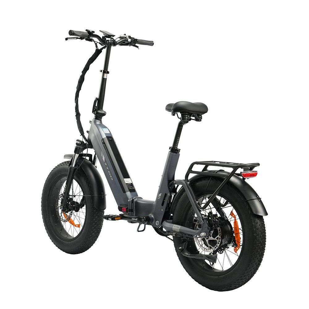Vélo électrique pliable gris avec pneus noirs et accents orange. Il possède un porte-bagages et des freins à disque hydrauliques.