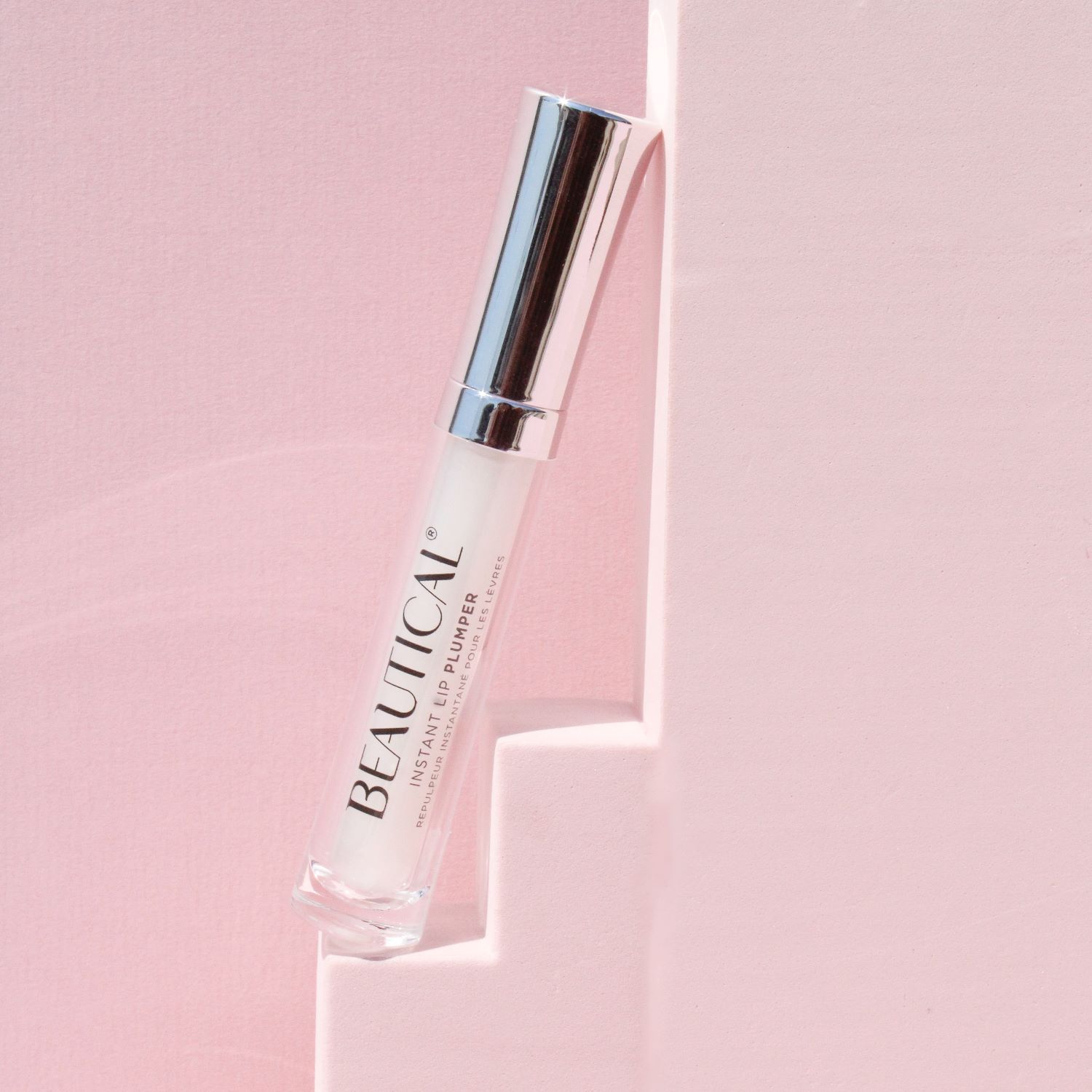 BEAUTICAL Instant Lip Plumper. Tube avec bouchon argenté, appuyé contre un mur rose. Applicateur blanc.