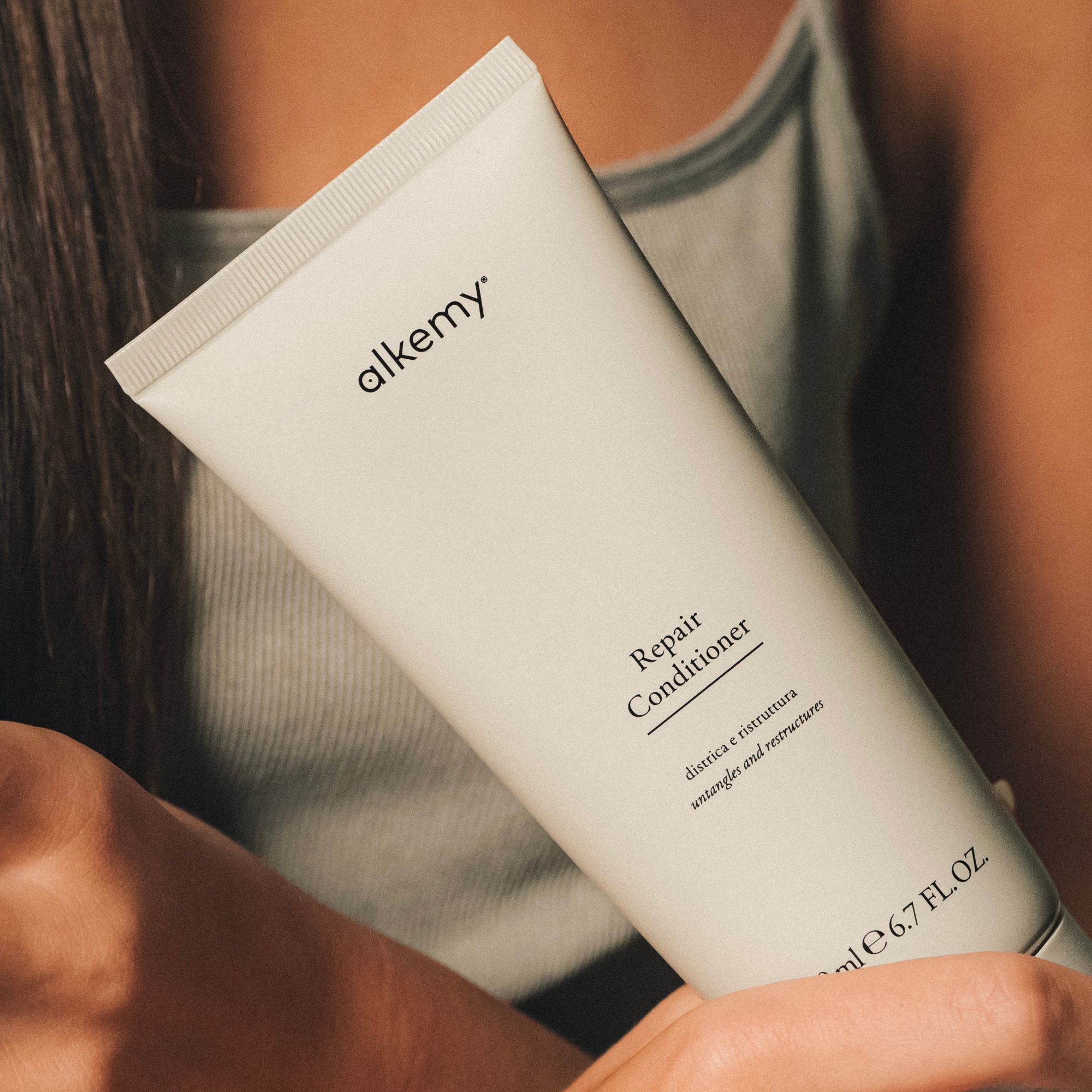 Un tube de revitalisant réparateur Alkemy, 200 ml, tenu par des mains.