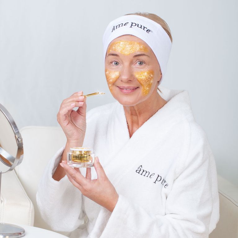 Femme avec masque doré et bandeau âme pure appliquant le gommage.