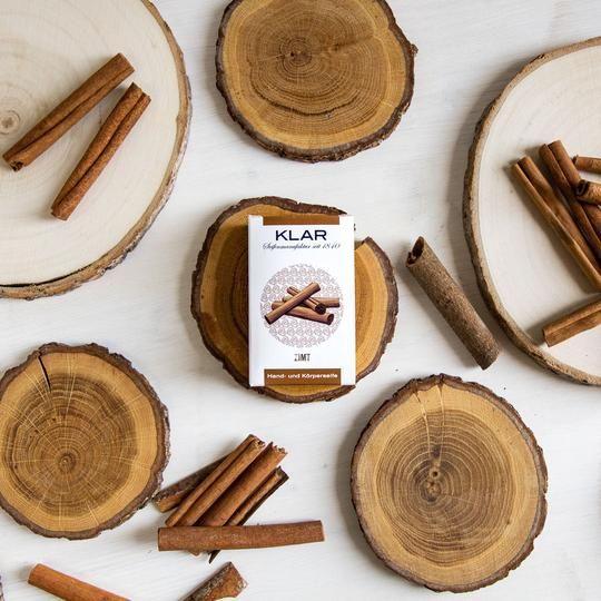 Productverpakking op een houten schijf, omringd door kaneelstokjes en andere houten schijven. Verpakking met kaneelillustratie en tekst KLAR.