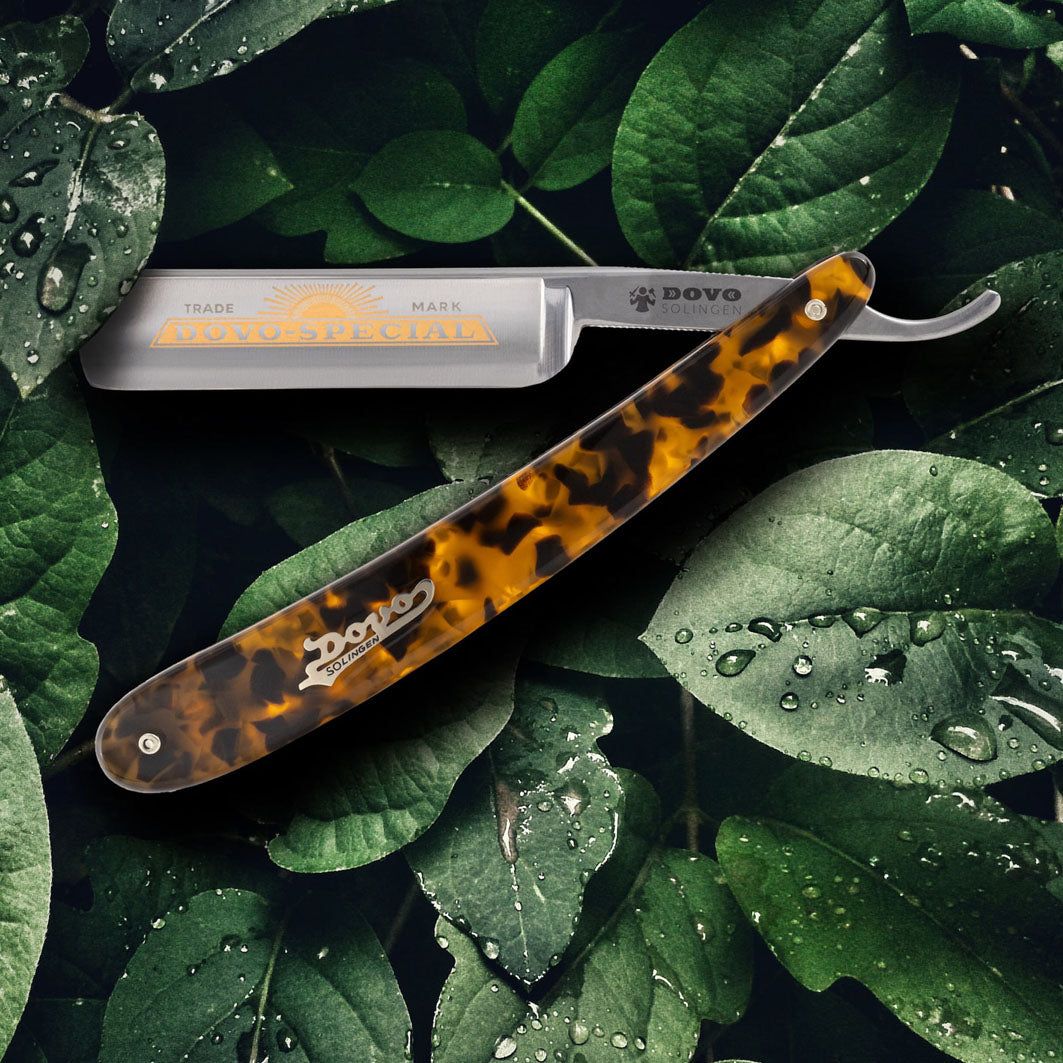 Rasoir DOVO SPÉCIAL avec manche imitation écaille de tortue. Lame avec logo et texte. Posé sur des feuilles.