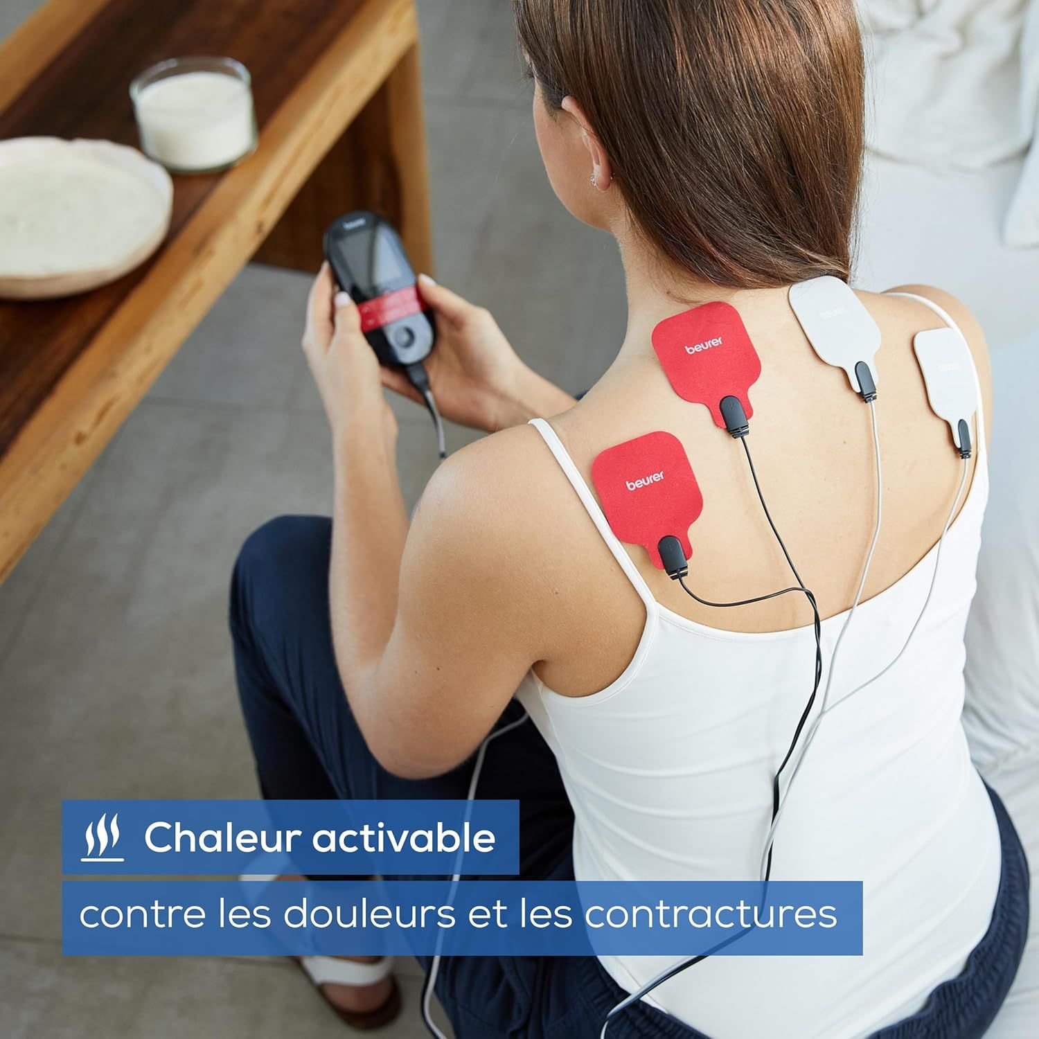 Femme avec électrodes TENS/EMS sur le dos, tenant la télécommande, symbole chaleur.