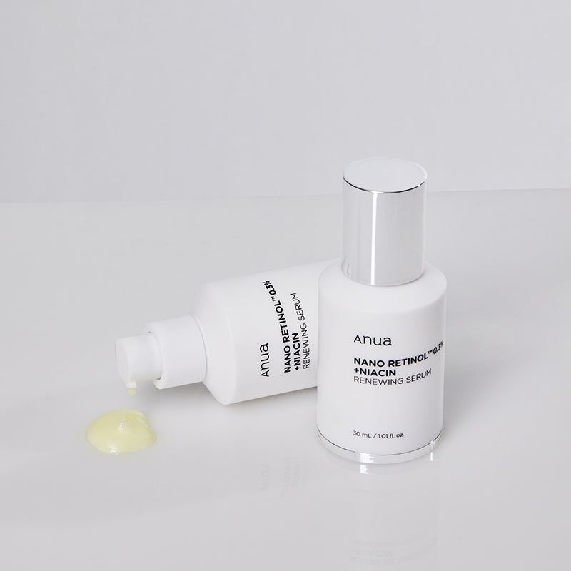 Twee witte flessen met zilveren doppen. Opschrift: Anua, Nano Retinol 0,3% + Niacin, Renewing Serum. Gele vloeistof ernaast.