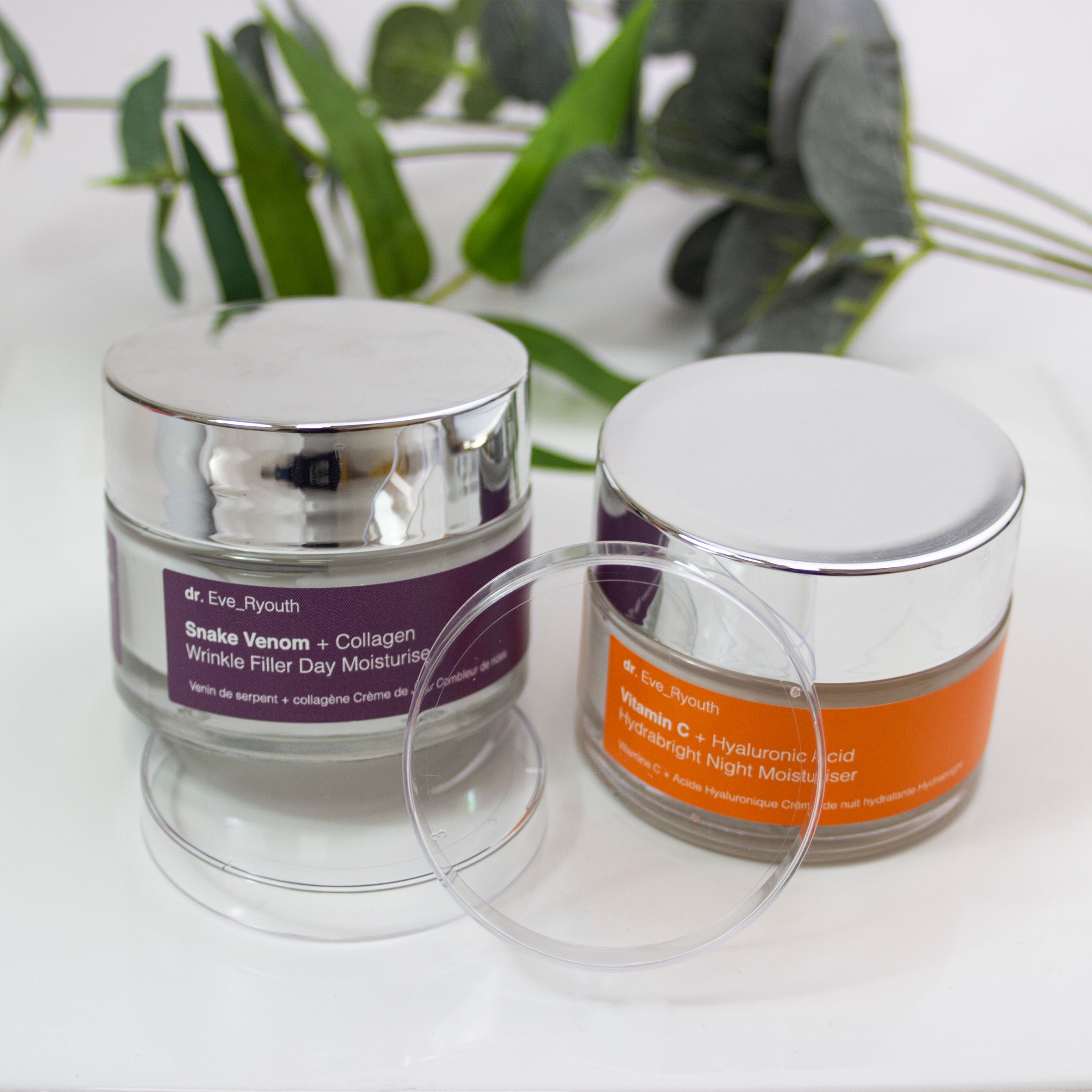 Deux pots de crème de jour et de nuit Dr. Eve_Ryouth sur une assiette blanche. Étiquettes violettes et orange. Couvercles argentés.