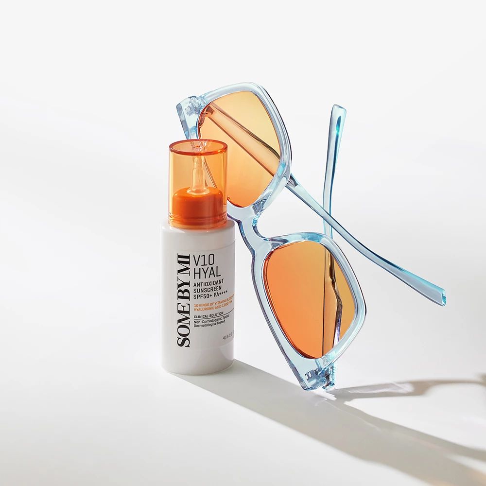 Flacon blanc avec bouchon orange à côté de lunettes de soleil bleues. Texte : V10 HYAL Antioxidant Sunscreen SPF50+.