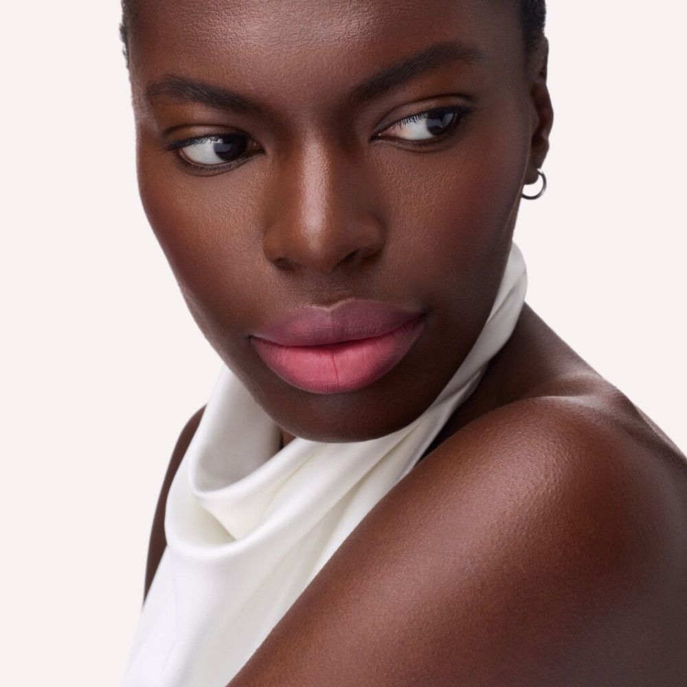 Portrait d'une personne portant du rouge à lèvres rose. La personne porte un haut blanc.