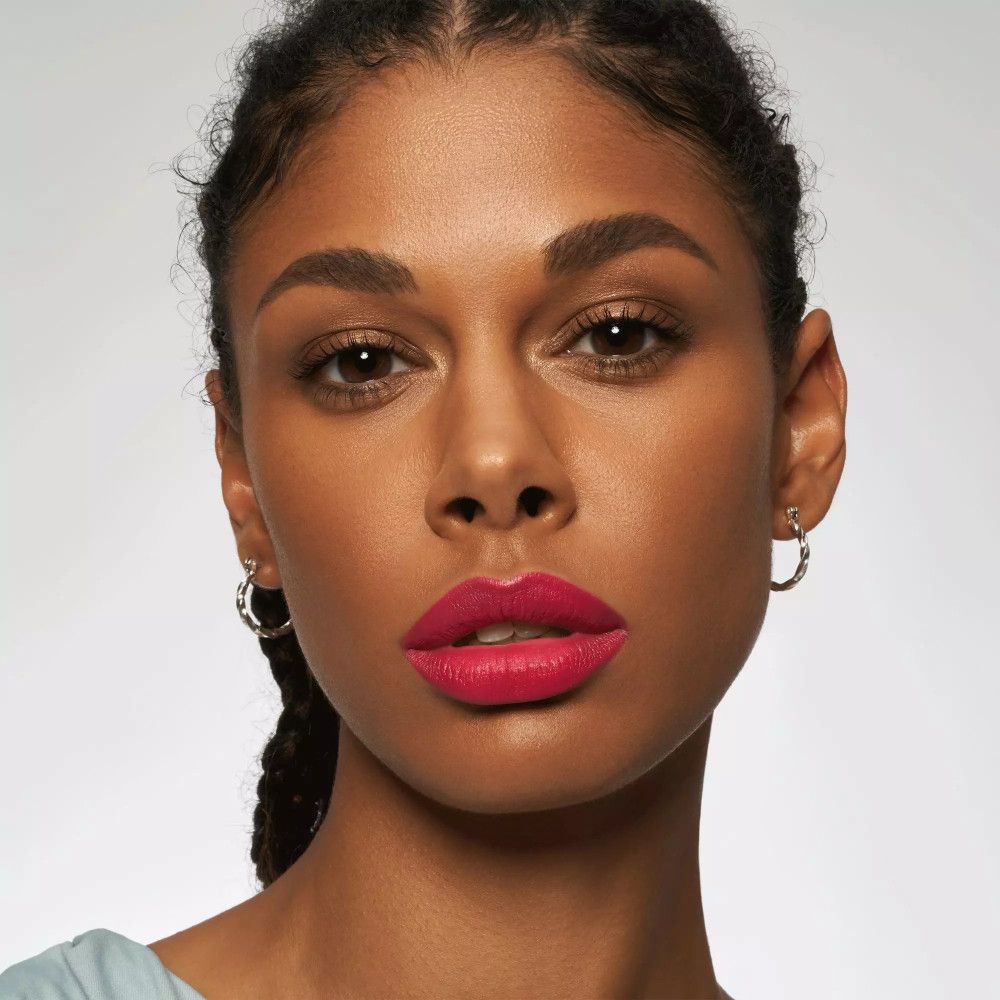 Portrait d'une femme avec du rouge à lèvres rose. Elle porte des boucles d'oreilles et regarde la caméra.