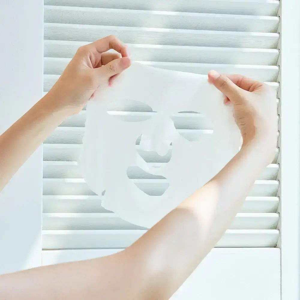 Handen houden een wit gezichtsmasker vast. Het masker heeft openingen voor ogen, neus en mond.