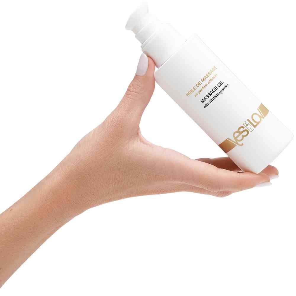 Witte fles massageolie met pompdos, vastgehouden in een hand. Bevat titillerende werkstoffen.