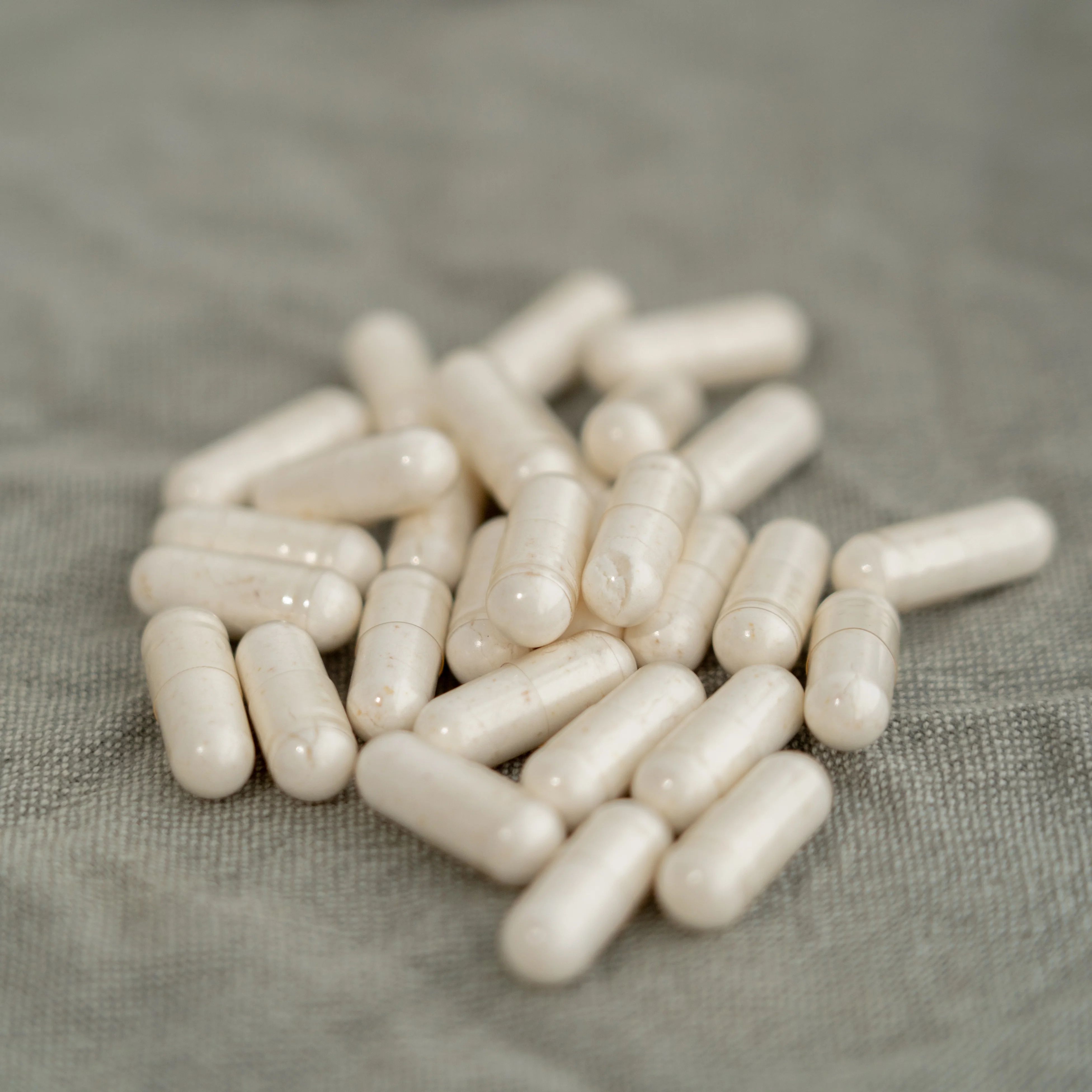 Stapel witte capsules. Capsules zijn langwerpig, doorschijnend en liggen op een grijze ondergrond.