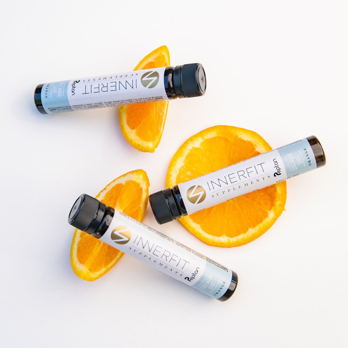 Trois ampoules en verre avec bouchon noir et tranches d'orange. Inscription : Innerfit Supplements, Collagen Shot, Orange. Logo doré.