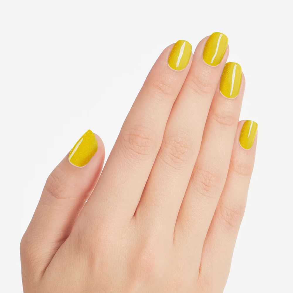 Main avec cinq ongles peints en jaune. Les ongles sont de forme ovale.