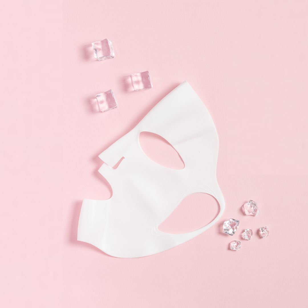 Wit siliconen masker op roze achtergrond. IJsblokjes ernaast. Masker heeft openingen voor ogen en mond.