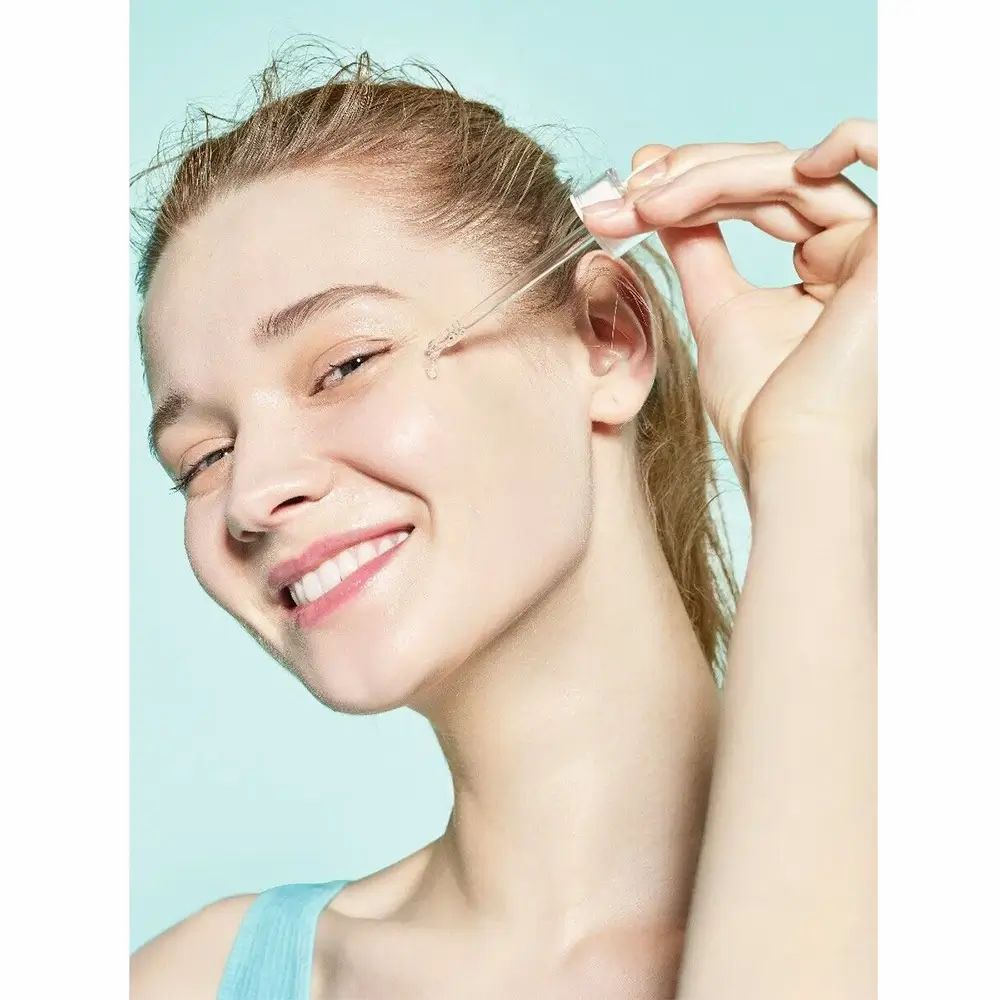 Vrouw met serum-applicator. Serum wordt op de huid aangebracht. Blauwe achtergrond.