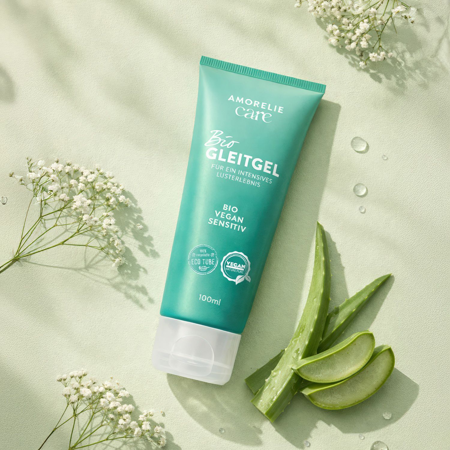 Groene tube met tekst en logo. Naast de tube liggen aloë vera bladeren en bloemen.