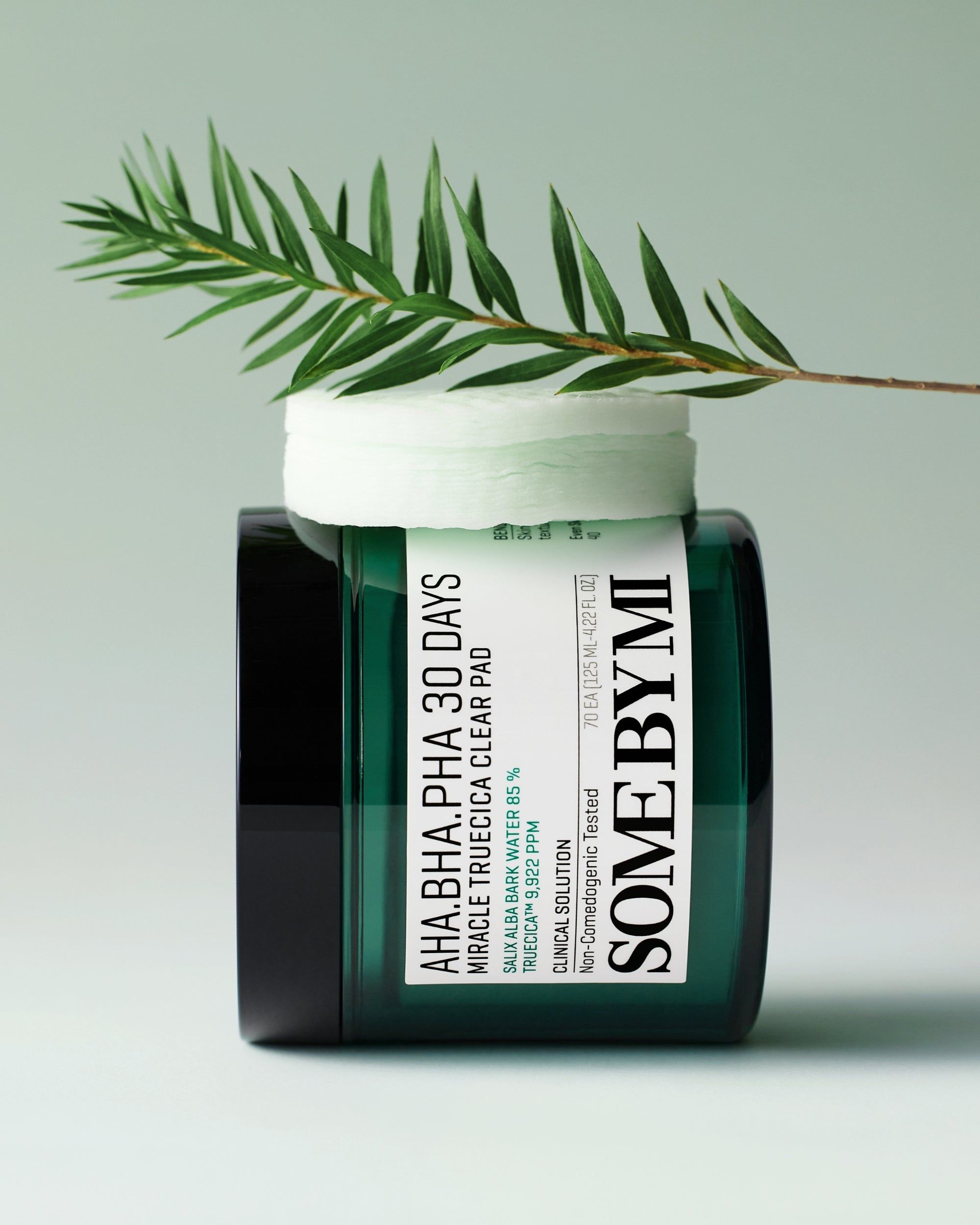 SOMEBYMI AHA-BHA-PHA Clear Pad dans un pot en verre vert avec couvercle et décoration de feuille.