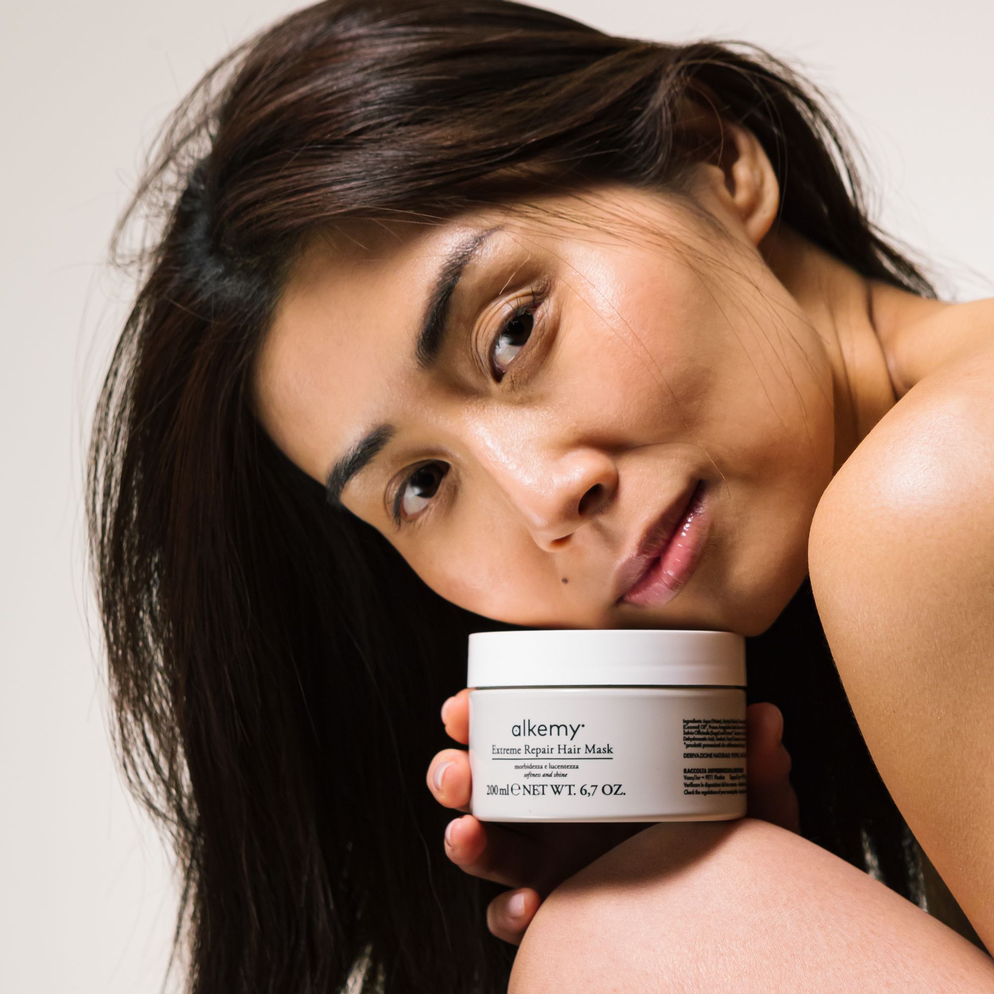 Masque capillaire Réparateur Intense Alkemy dans un pot crème, tenu par une femme.