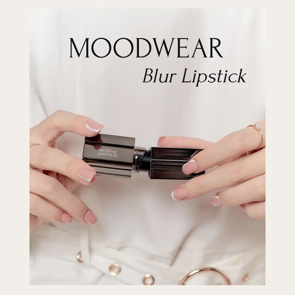 Handen houden een lipstick vast. Zwarte huls met zilveren details. Opschrift: MUZIGAE MANSION. Tekst: MOODWEAR Blur Lipstick.