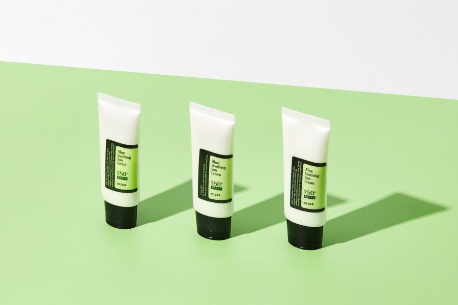 Drie witte tubes met zwarte dop. Etiketten met productinformatie. Tekst: Aloe Soothing Sun Cream SPF50+ PA+++.