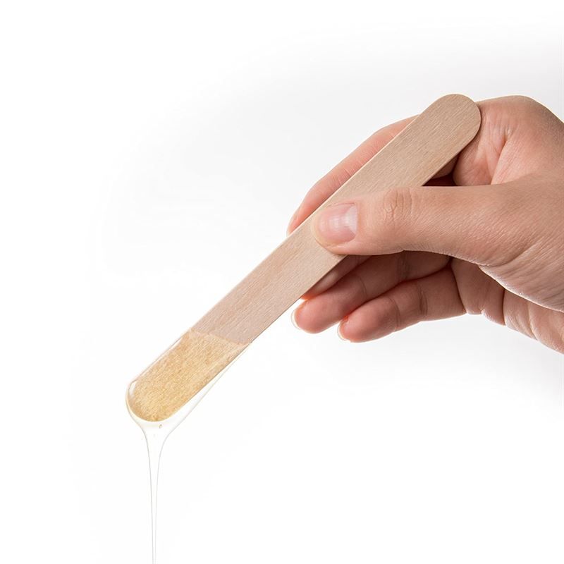 Hand die een houten spatel met wax vasthoudt.