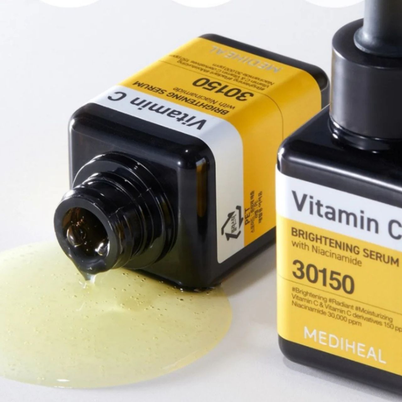 Deux flacons de sérum Mediheal Vitamine C, l'un renversé laissant échapper du sérum. Étiquettes jaunes avec inscription noire.