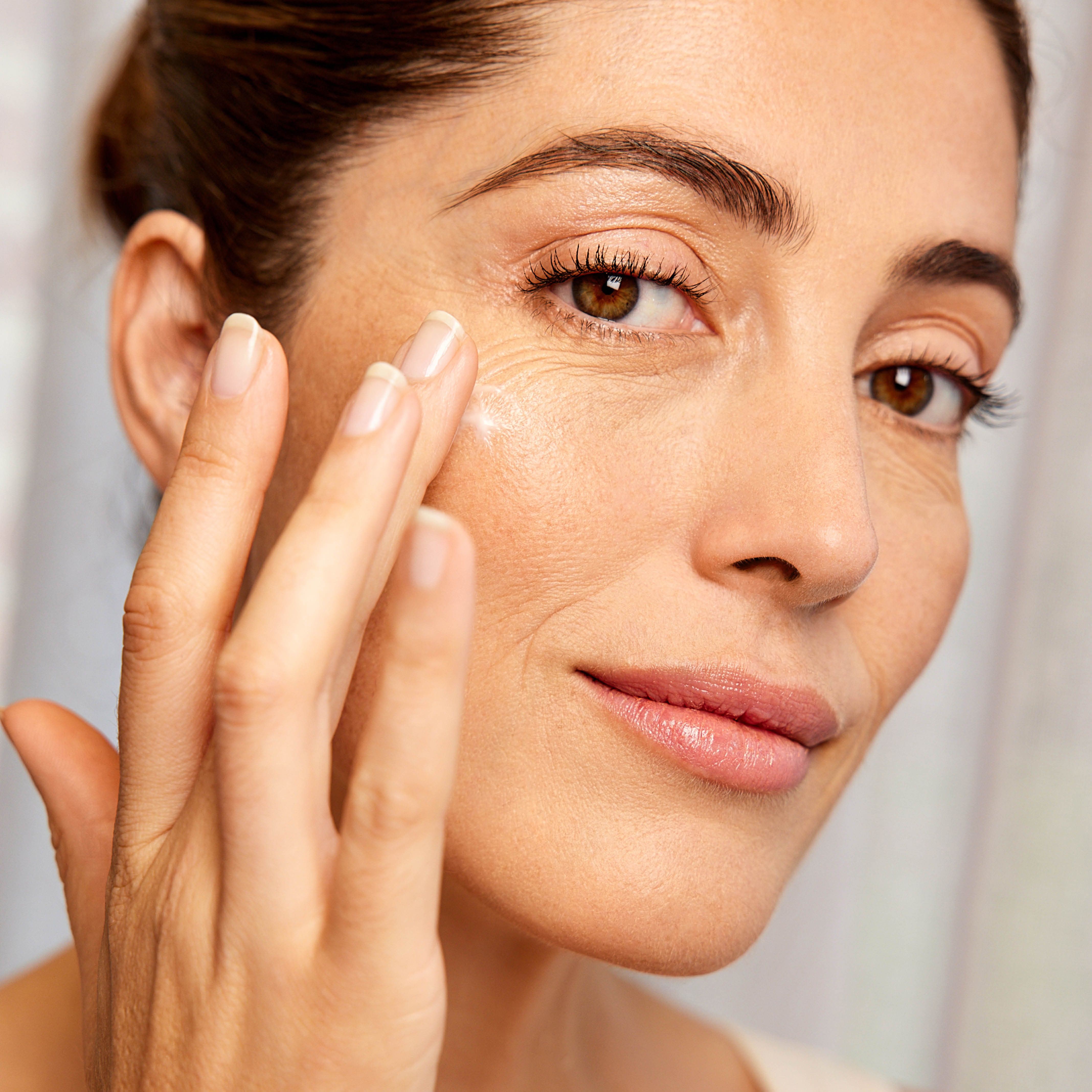 Femme appliquant de la crème. Gros plan. Pas d'emballage produit visible. Femme touchant son visage.