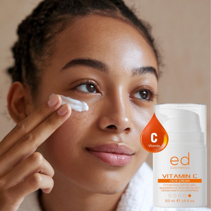 Jeune femme appliquant de la crème. Flacon blanc avec étiquette orange. Texte : Vitamin C Face Cream, ed cosmetics.