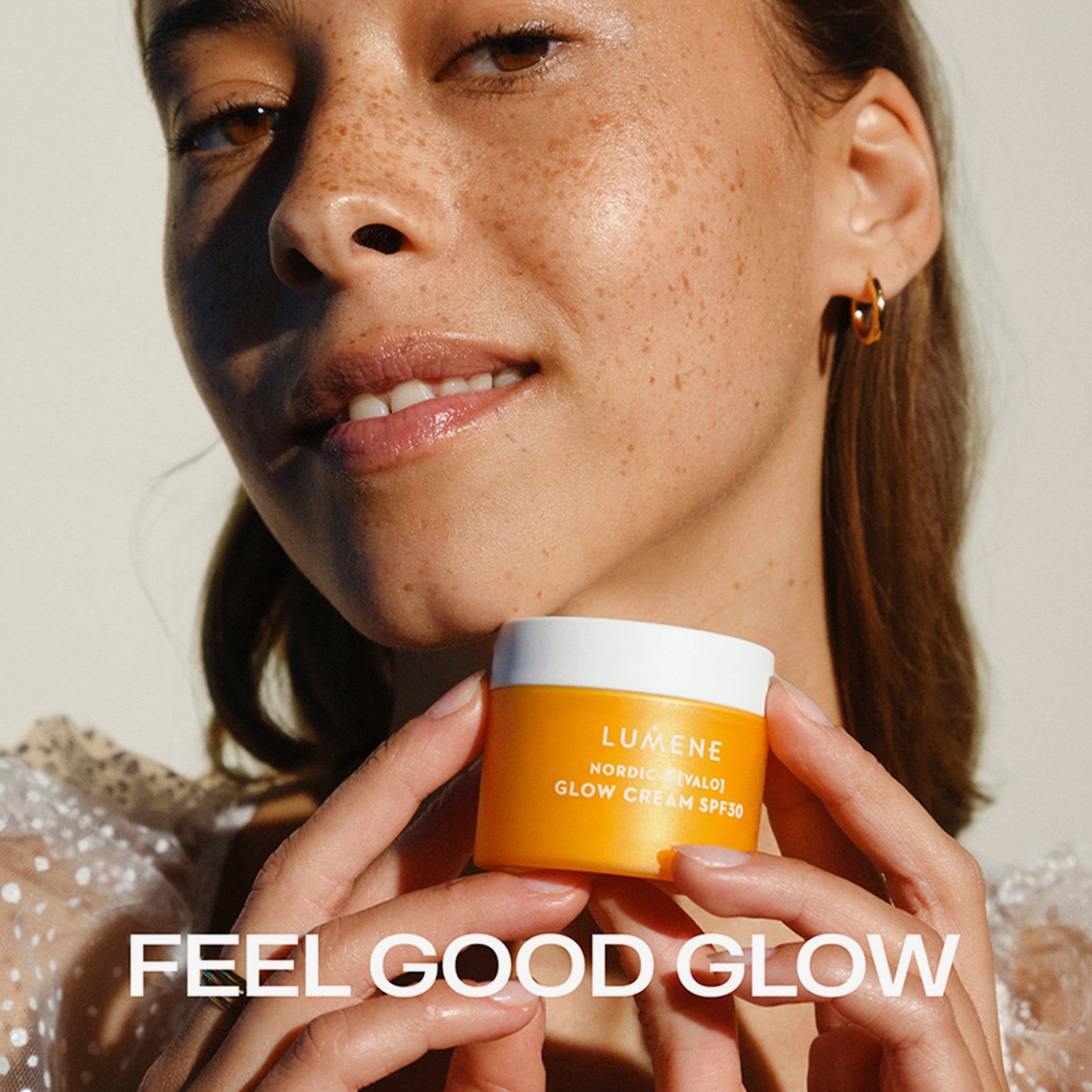 Femme tenant un pot de crème jaune. Inscription : LUMENE, NORDIC-C [VALO] GLOW CREAM SPF30. Texte : FEEL GOOD GLOW.