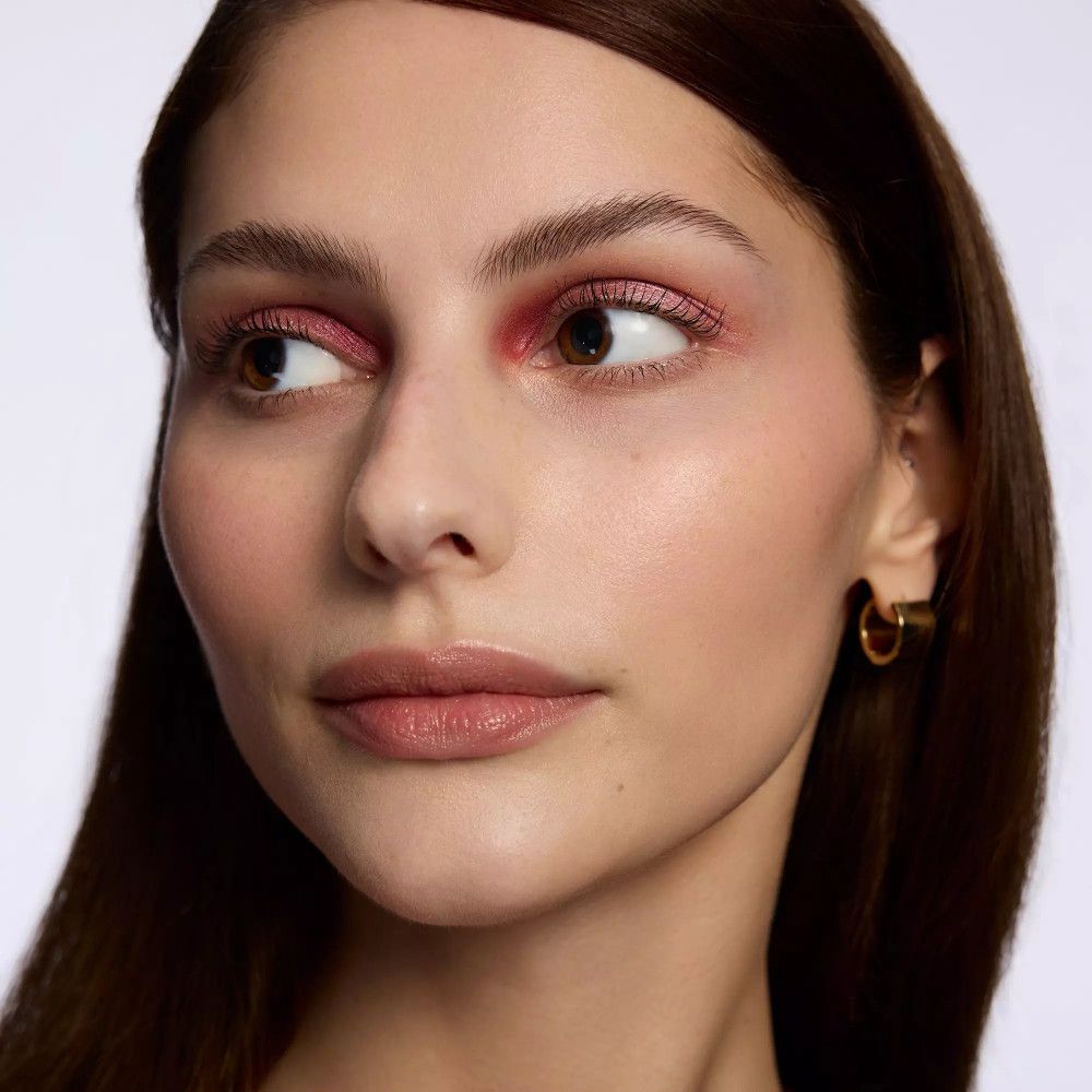 Gros plan d'un visage avec fard à paupières rose et boucles d'oreilles dorées.