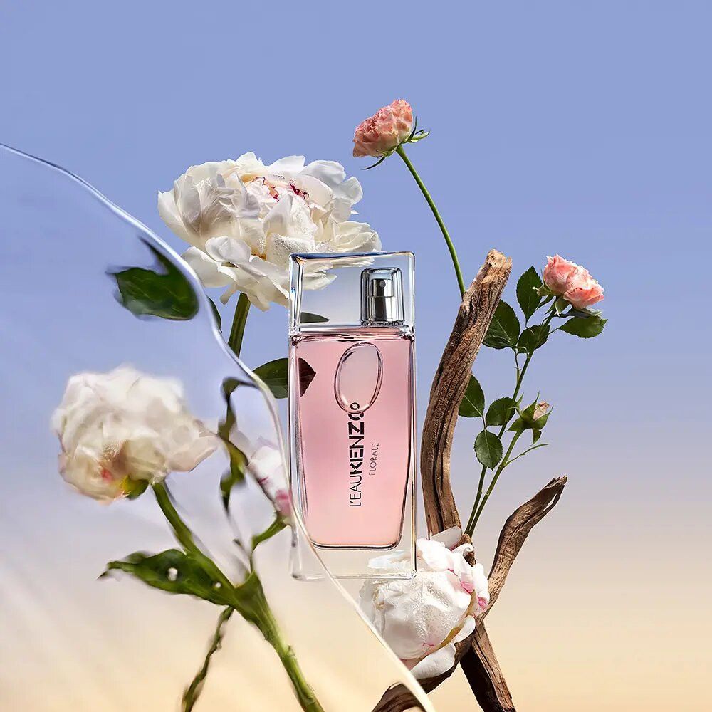 Fles met bloemarrangementen. Fles: rechthoekig, roze vloeistof. Bloemen: witte pioenrozen, roze rozen. Achtergrond: blauw.