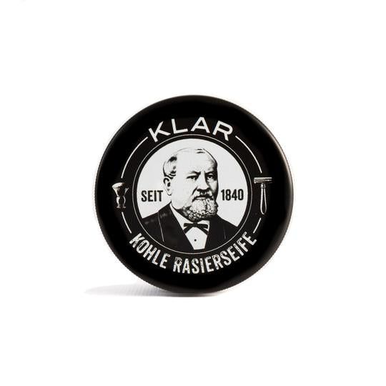 Savon à raser au charbon actif en boîte noire. Couvercle avec logo et portrait. Inscription: KLAR, KOHLE RASIERSEIFE, SEIT 1840.
