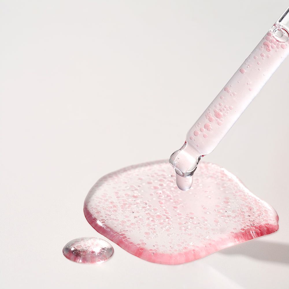 Serum met roze deeltjes druppelt uit een druppelaar op een oppervlak.