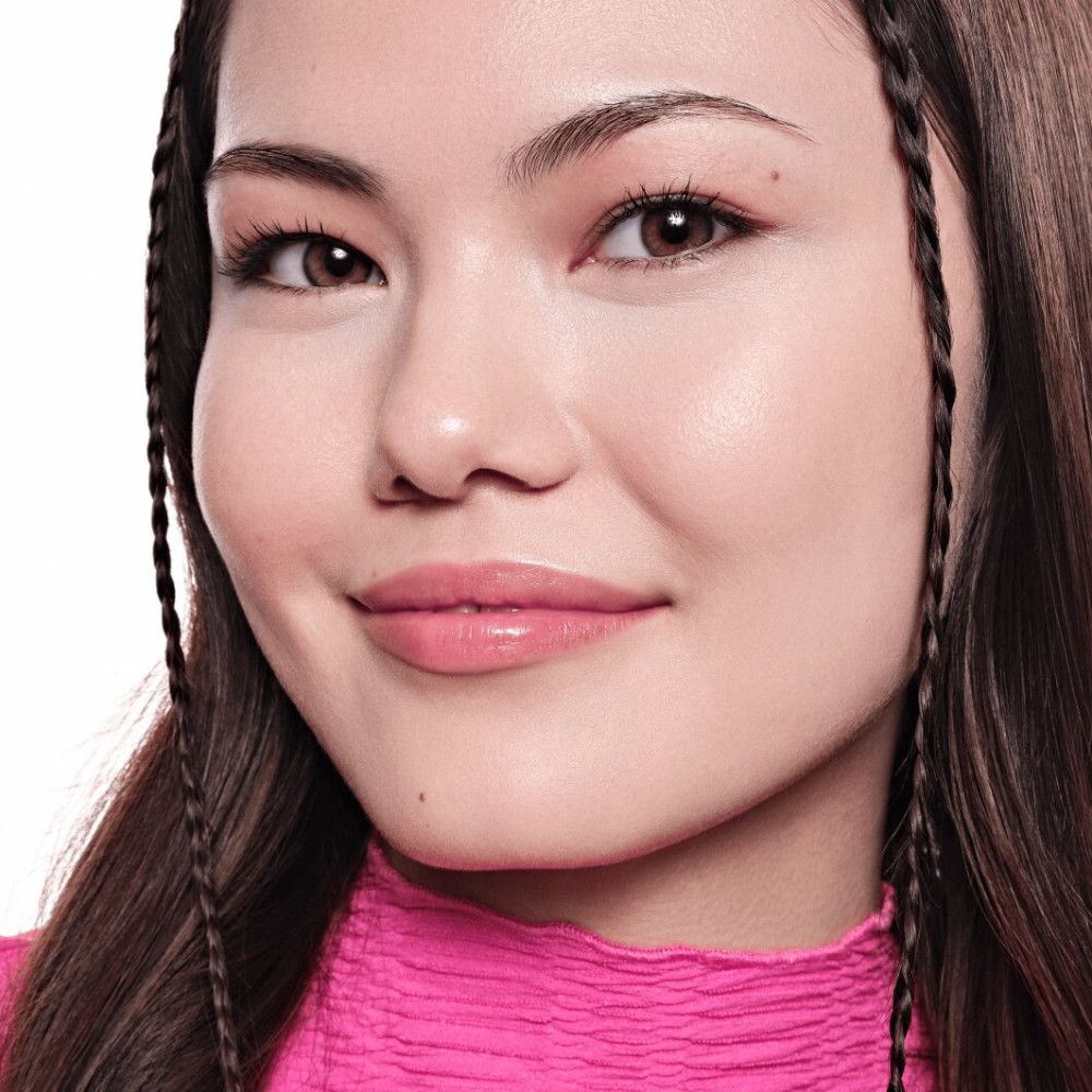 Gros plan d'un visage. La personne porte un haut rose et du maquillage. Visible : sourcils, lèvres, peau. Cheveux tressés.