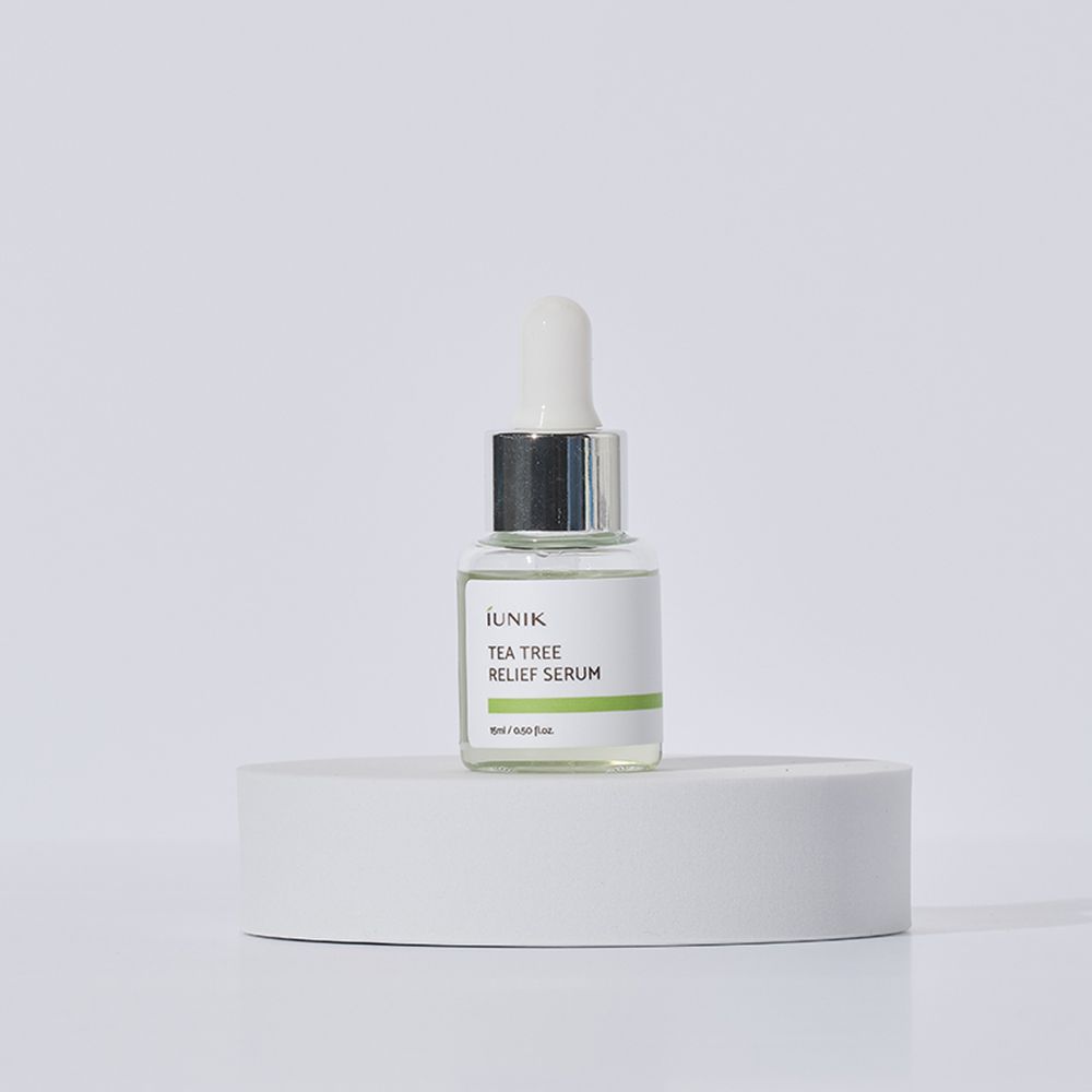 Sérum en flacon de verre avec pipette sur socle blanc. Étiquette blanche avec bande verte et texte: iUNIK TEA TREE RELIEF SERUM.