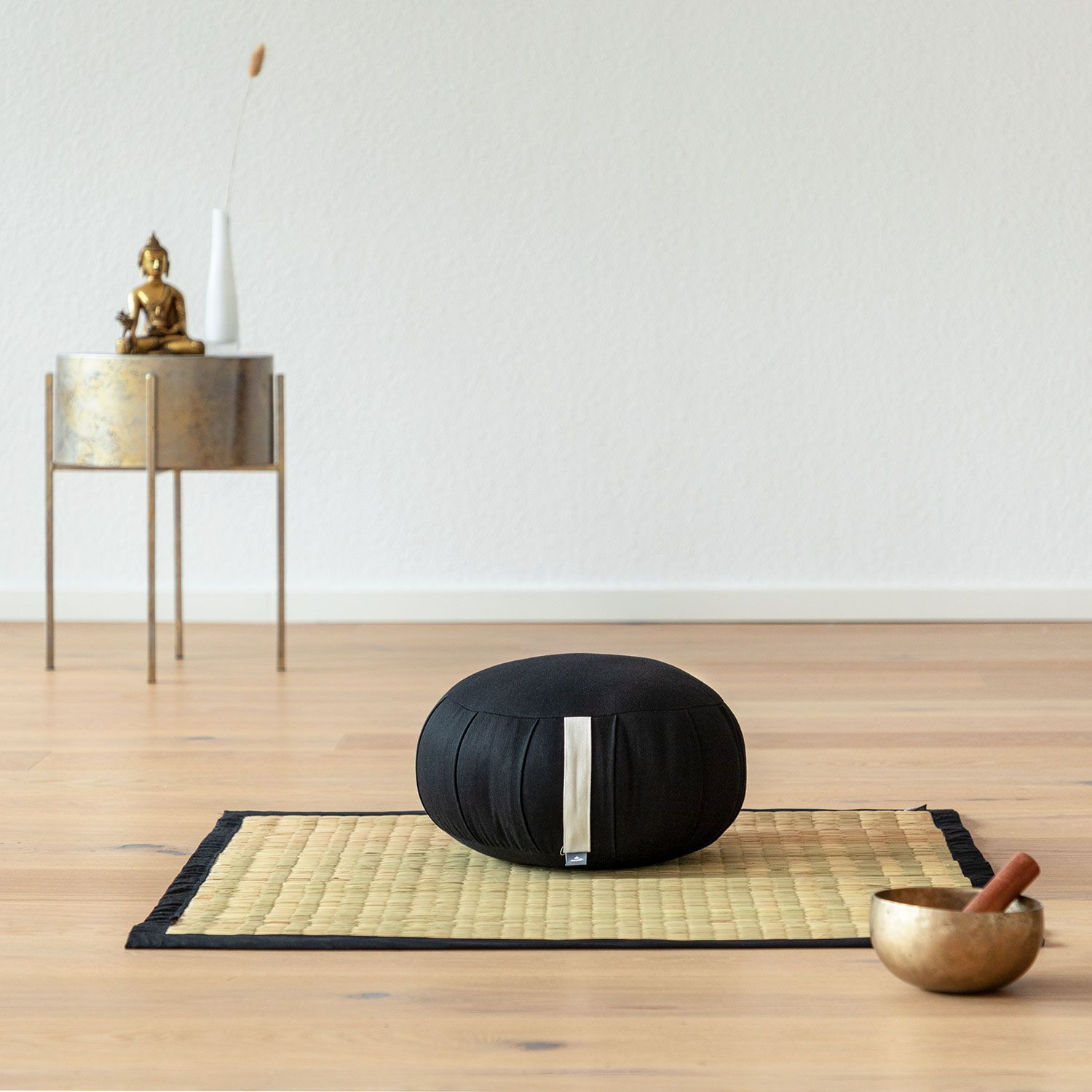 Tatami-mat met zwarte rand op houten vloer, met kussen en kom ernaast.