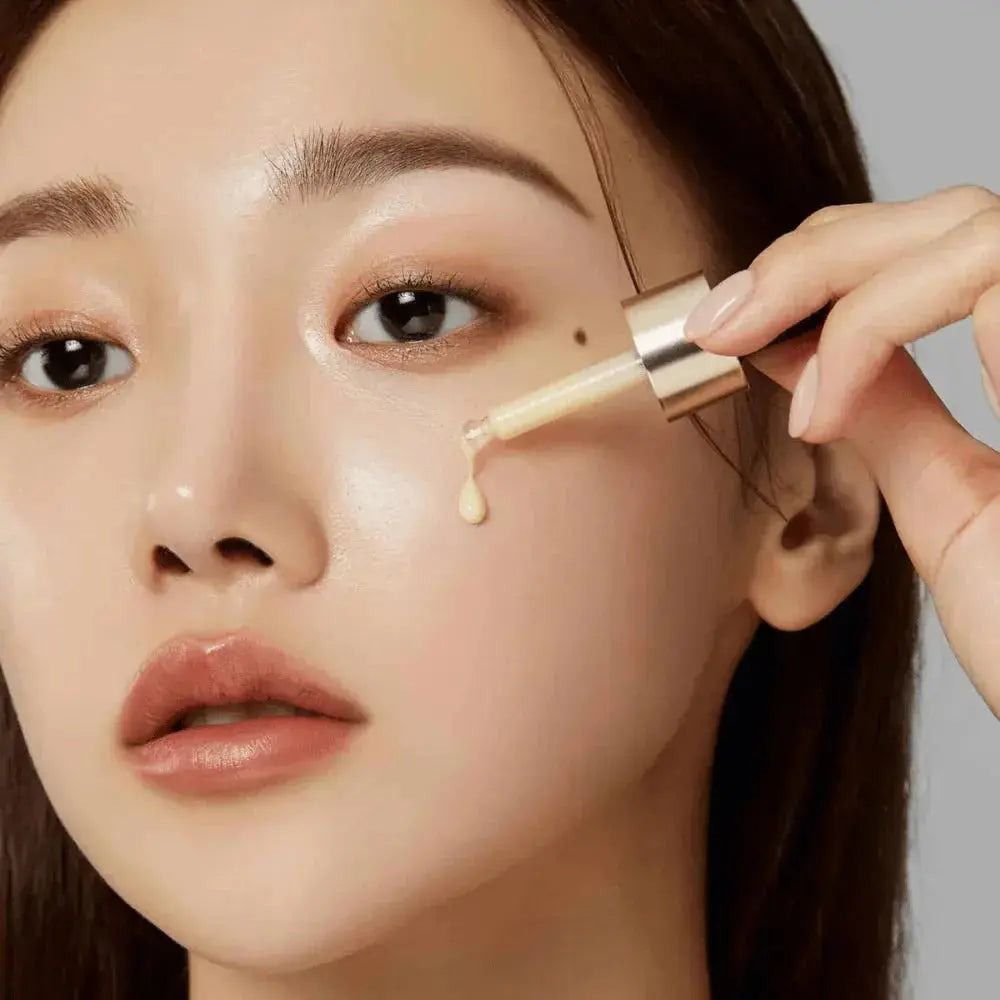 Close-up van een vrouw die serum met een pipet op haar gezicht aanbrengt. Huid glanst. Gouden pipet.