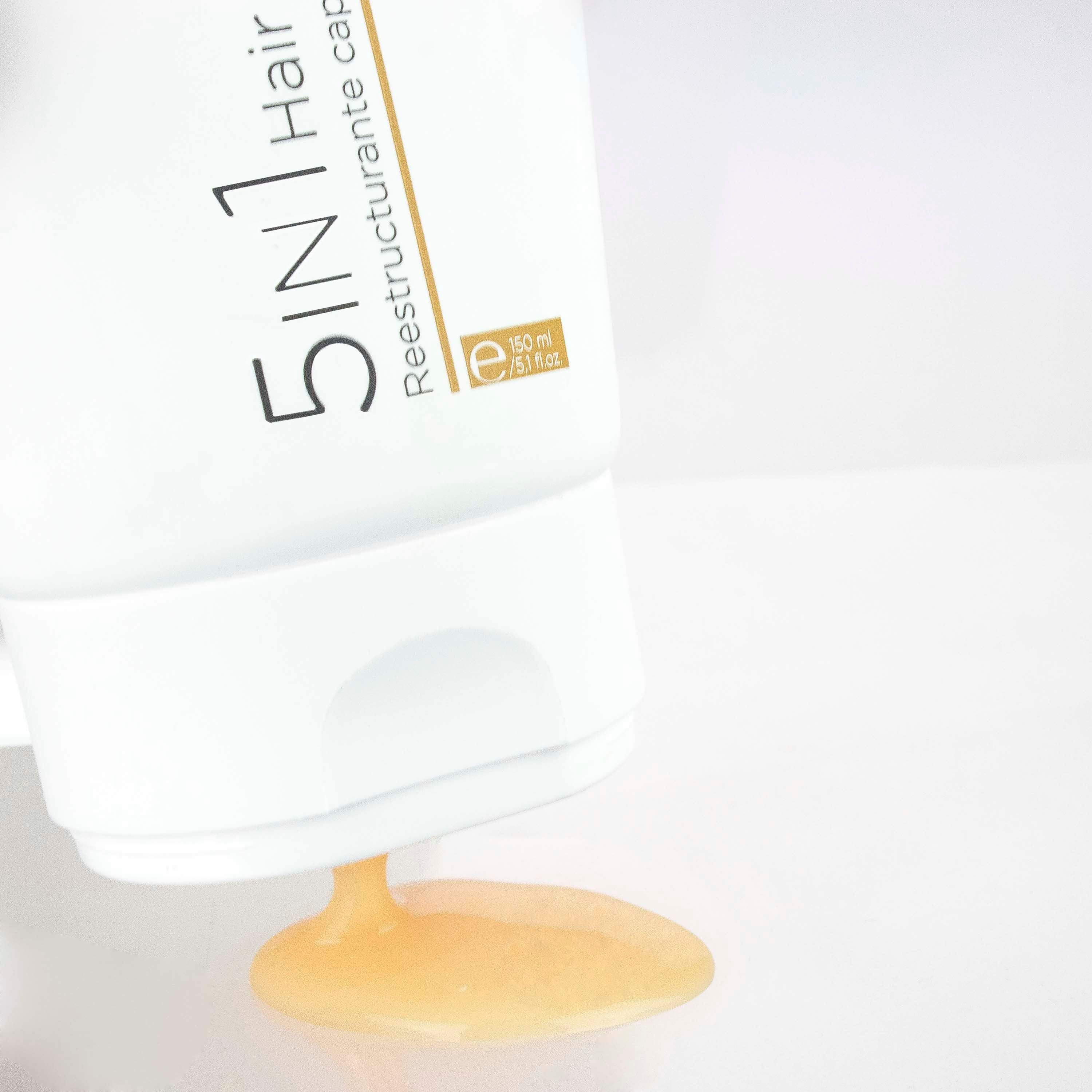 Witte tube, product wordt uitgegoten. Tekst: 5 in 1 Hair Restorer. Merk: Postquam. Gele vloeistof.