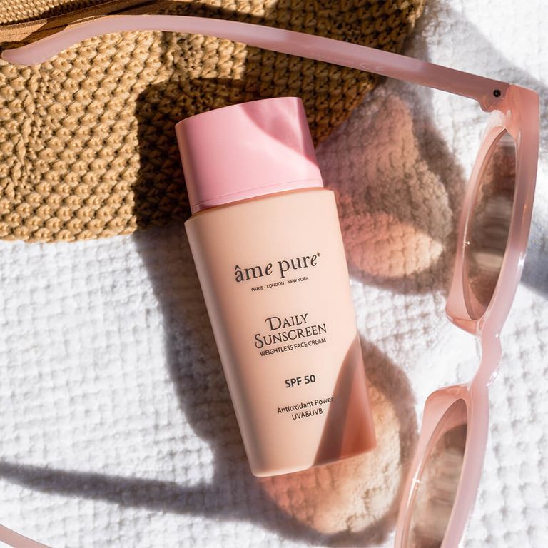 Crème solaire SPF 50 sur une serviette à côté de lunettes de soleil et d'un chapeau.