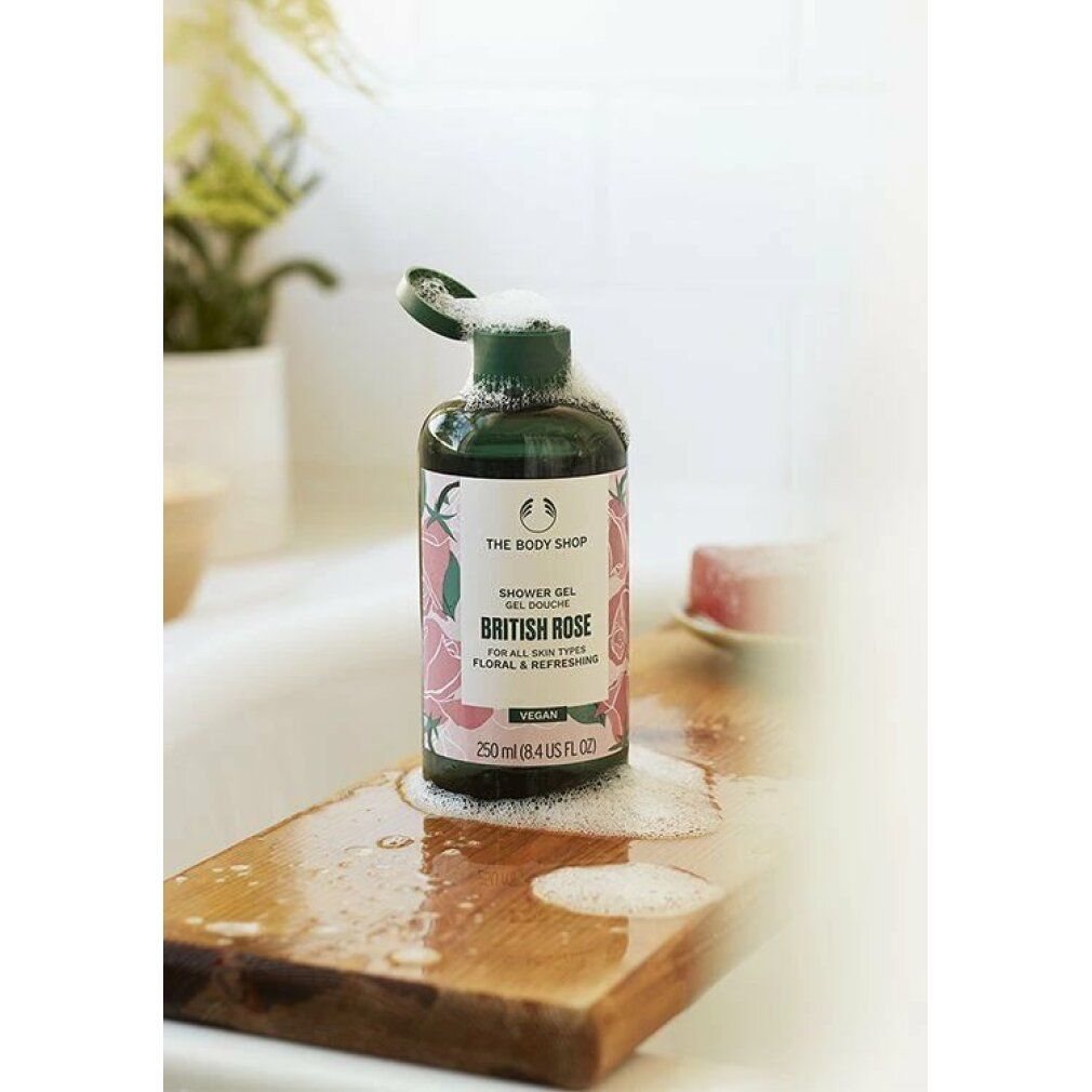 Flacon de gel douche British Rose sur planche en bois dans un lavabo. Mousse. Bouchon vert, étiquette blanche avec motif floral. Vegan.