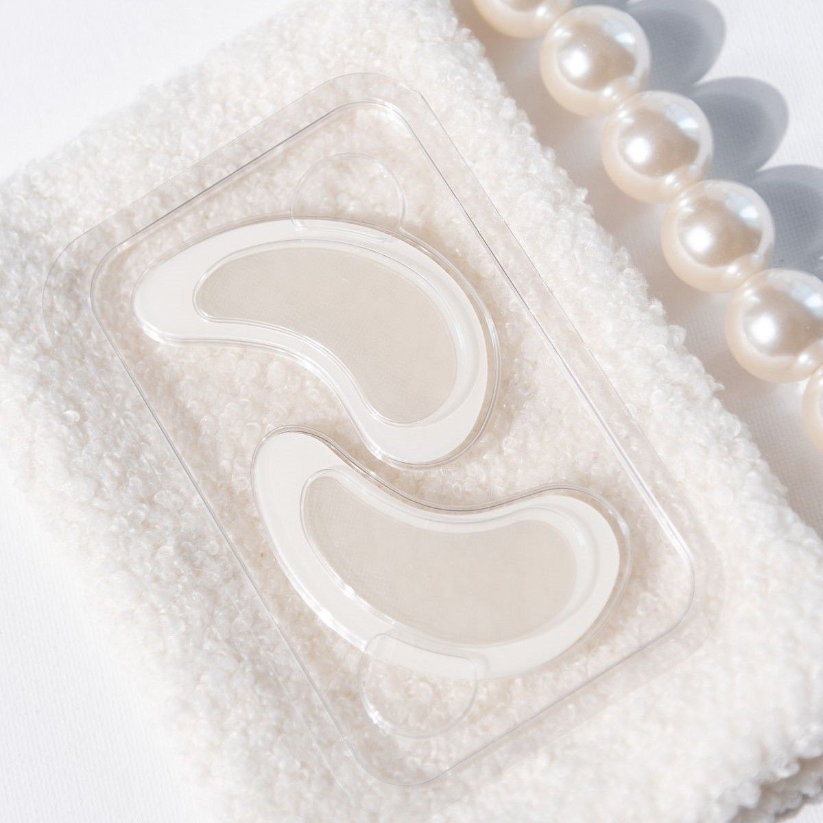 Deux patchs pour les yeux dans un emballage transparent. Sur une serviette blanche avec des perles.