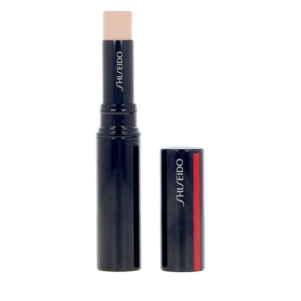Correcteur de teint en bâton. Bâton bleu foncé avec produit beige. Capuchon à côté. Logo Shiseido sur le bâton et le capuchon. Bande rouge sur le capuchon.