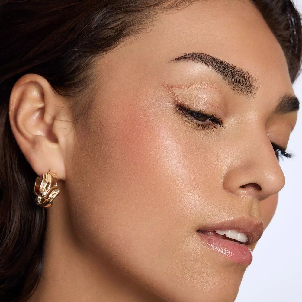 Gros plan d'une femme avec des boucles d'oreilles dorées. Elle a la peau foncée et porte du maquillage.