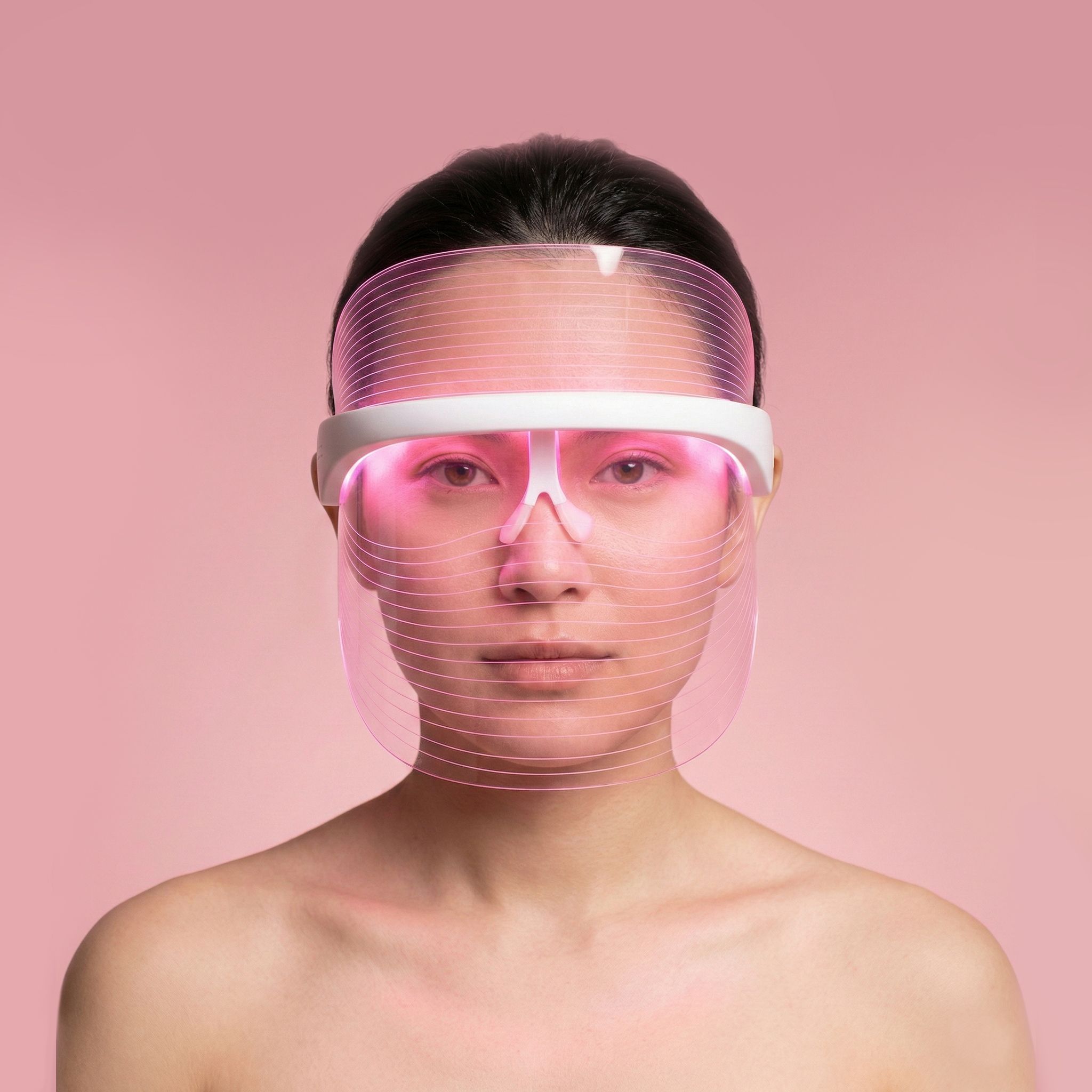 Vrouw met een lichtgevend roze LED-gezichtsmasker.