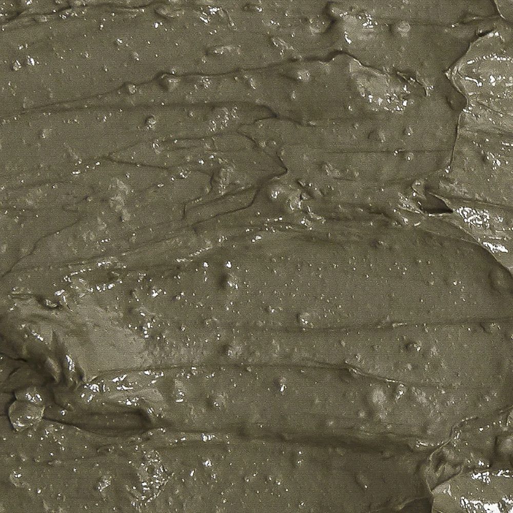 Texture d'un masque à l'argile gris-vert avec des stries et des ondulations visibles.
