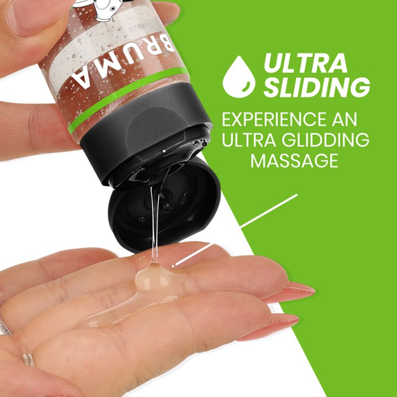 Een hand houdt een fles Bruma massageolie vast, met olie die op de andere handpalm druppelt.