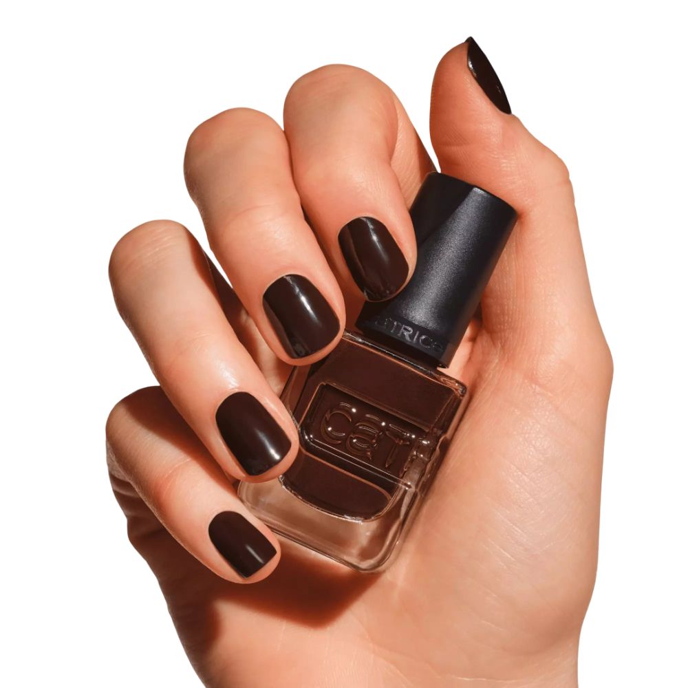 Main tenant un flacon de vernis à ongles. Ongles vernis en marron. Marque Catrice visible.