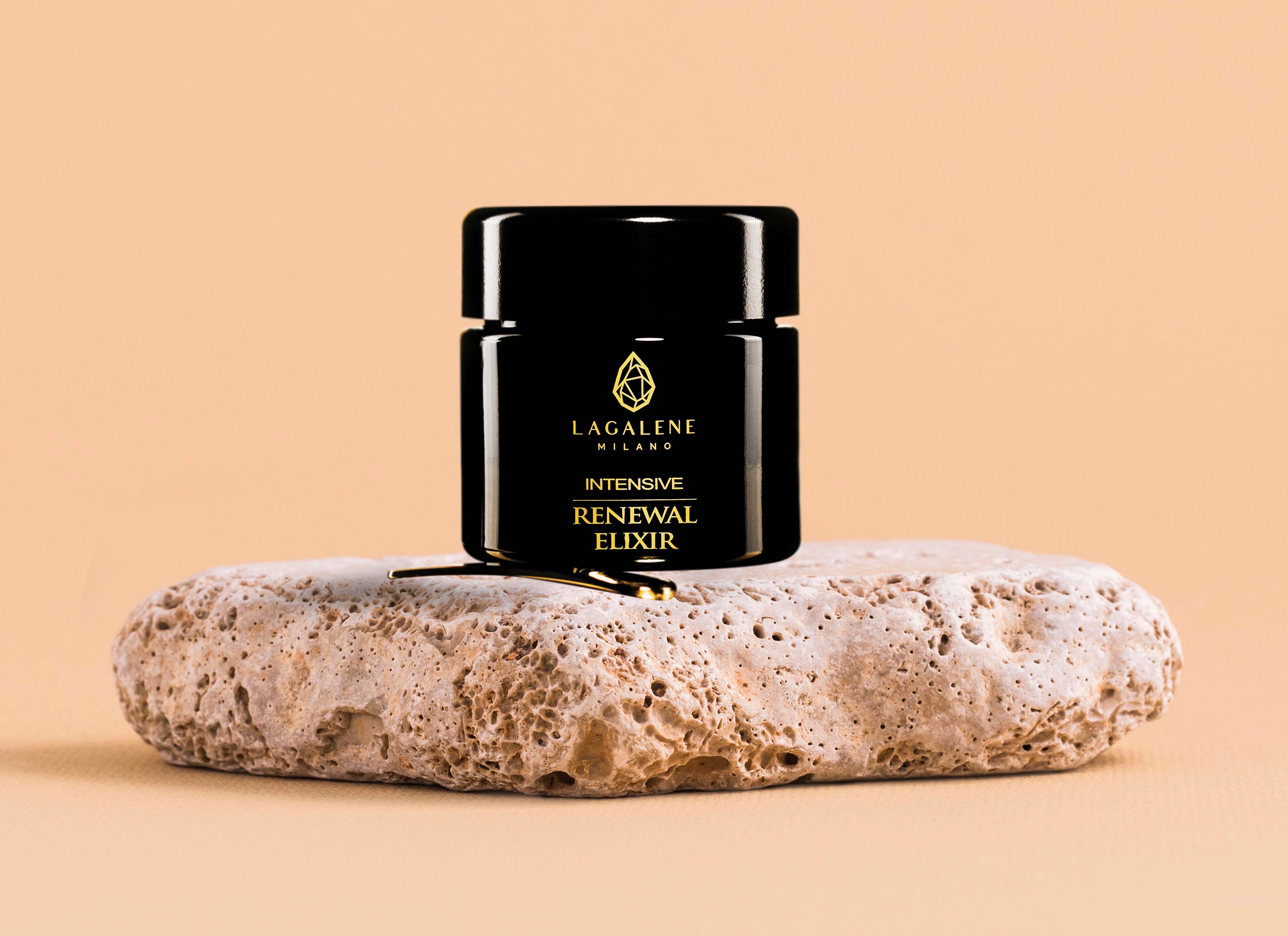 Pot noir avec texte et logo dorés sur pierre. Texte: Intensive Renewal Elixir. Spatule dorée.